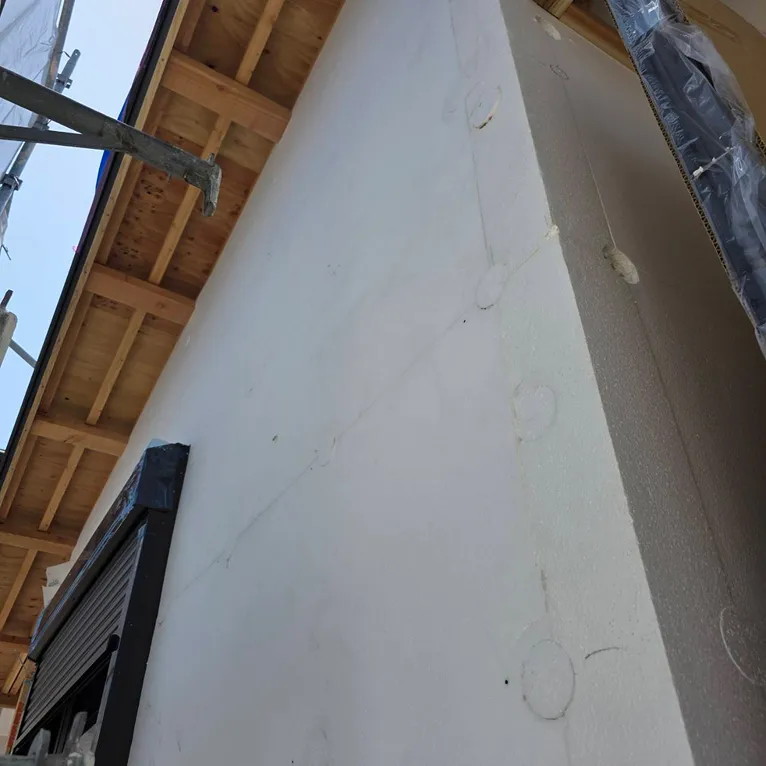 建設中の建物の外壁を下から見上げた角の部分、木製の屋根裏も見える。
